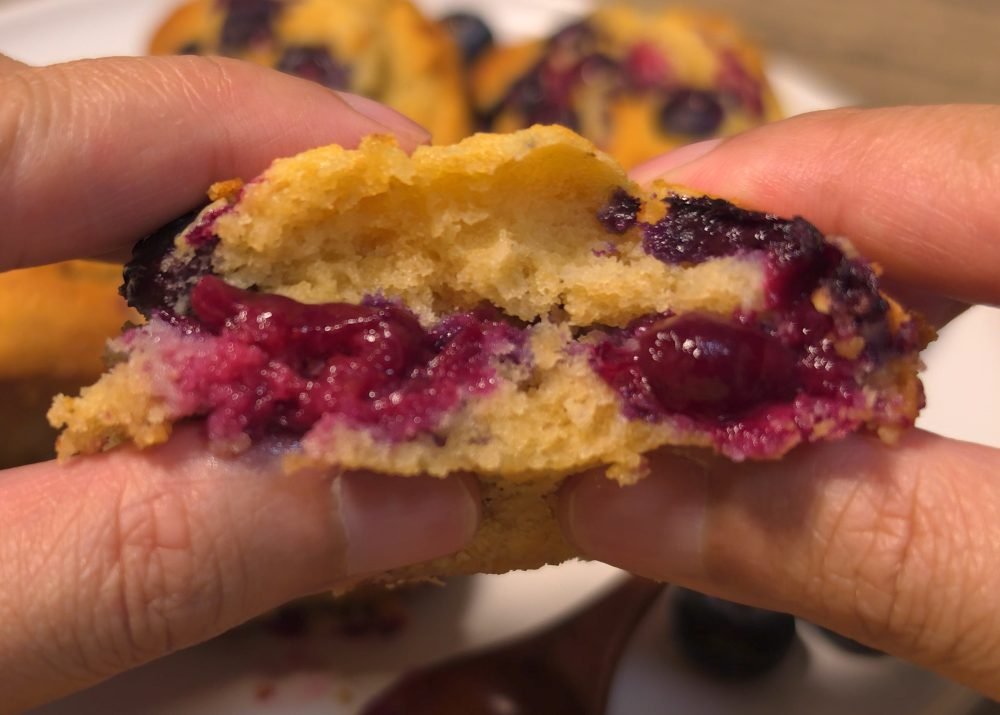Hand pulling apart a soft air fryer mini blueberry cake with bursting berries