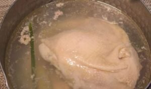 Chicken thigh steeping in the poaching broth with spring onion