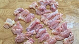 Chicken thigh cut into bite-sized pieces on a wooden board