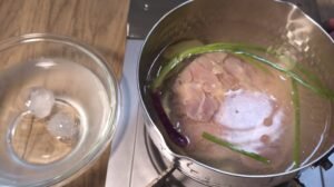 Chicken dipped into the poaching pot beside a bowl of ice water