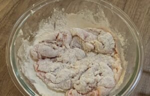Marinated chicken thigh coated in flour in a glass bowl