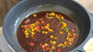 Gochujang glaze simmering with diced bell peppers in a pan
