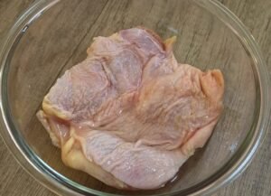 Chicken thigh marinating in sake in a glass bowl
