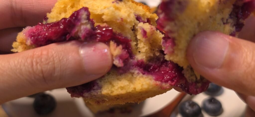 Two hands pulling apart a soft air fryer mini blueberry cake with jammy berries inside