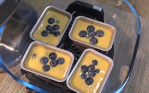 Four mini loaf pans filled with batter and topped with blueberries in the air fryer
