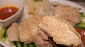 Poached chicken rice plated with sliced chicken, cucumber and chili dip
