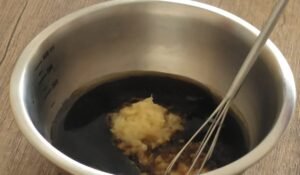 Soy garlic marinade with grated garlic being whisked in a steel bowl