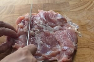 Butterflying a boneless chicken thigh on a wooden cutting board