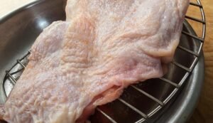 Salted chicken thigh on a wire rack, ready to dry brine uncovered overnight