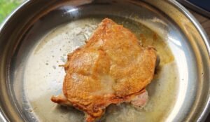 Chicken thigh searing skin side down in a stainless steel pan until golden