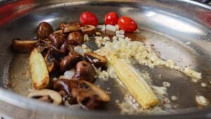 Mushrooms, baby corn and cherry tomatoes with butter, garlic and onion in the pan