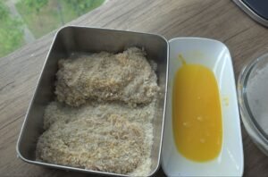 Chicken thigh pieces coated in panko beside a dish of beaten egg