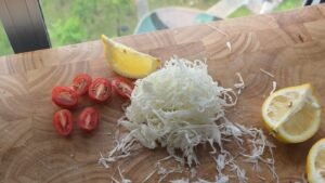 Finely shredded cabbage, halved cherry tomatoes and lemon wedges on a cutting board